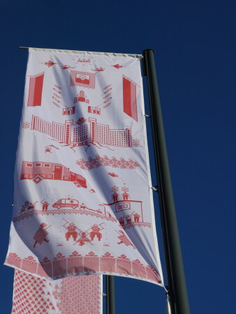 Die belarussische Knstlerin Rufina Bazlova zeigt auf drei Fahnen vor dem neuen Minsk Bilder der politischen Unruhen in ihrer Heimat in traditionellen Kreuzstick-Mustern.