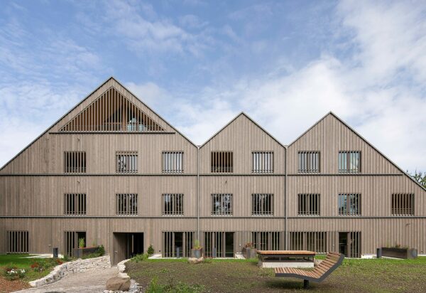 Der kompakte Baukörper wird von mehreren Satteldächern und einer vertikal orientierten Holzfassade geprägt.