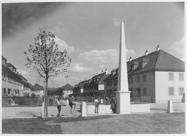 Hannes Meyer: Siedlung Freidorf in Muttenz, Schweiz. Brunnen mit Obelisk und Wohnhof, umgeben von Husern mit eigenem Nutzgarten, Fotografie von 1919