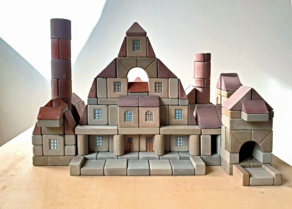 Steinbaukasten Bauhtte, Fuchs & Beug, DE (Bayern) 1920er und 1950er Jahre: Der Steinbaukasten steht in der Tradition der Anker-Bauksten, die ab 1884 produziert wurden. Die Elemente solcher Ksten sind aus verschiedenen Naturprodukten zusammengesetzt und fhlen sich daher an wie echter Stein.